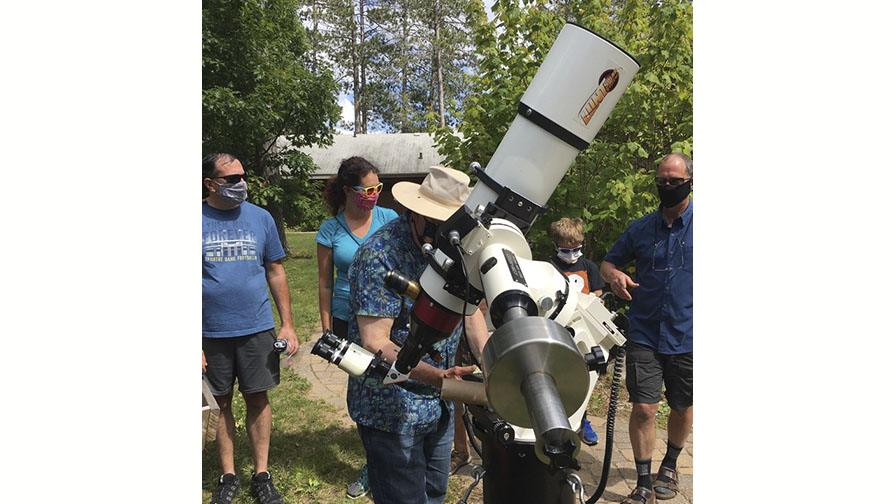 photo of a man looking through a telescope in the daytime while others look on